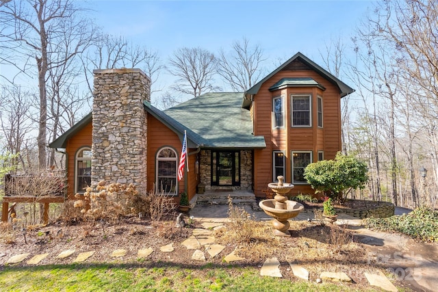 view of front facade featuring stone siding, roof with shingles, and a chimney