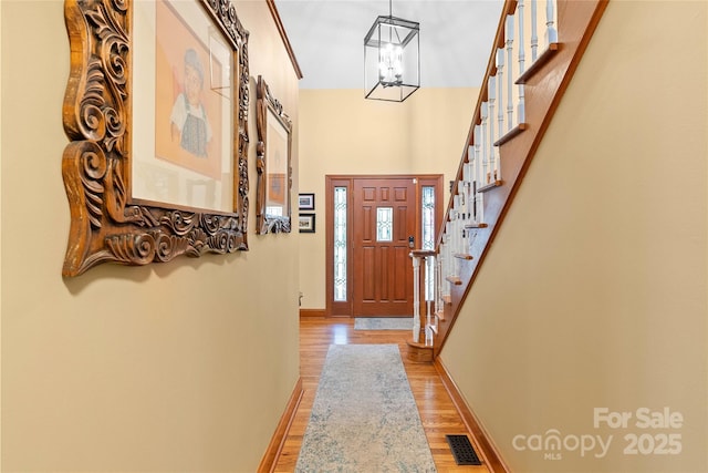 entrance foyer with visible vents, stairway, light wood-style floors, a chandelier, and baseboards