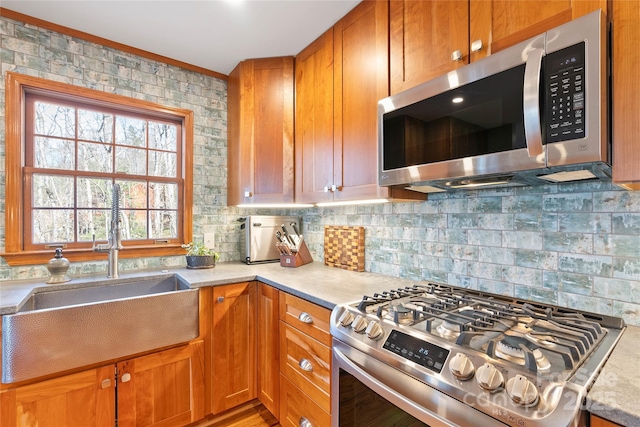 kitchen featuring light countertops, appliances with stainless steel finishes, brown cabinetry, and a sink