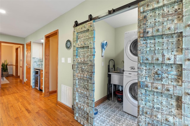 washroom featuring visible vents, a barn door, stacked washer / dryer, light wood-type flooring, and laundry area