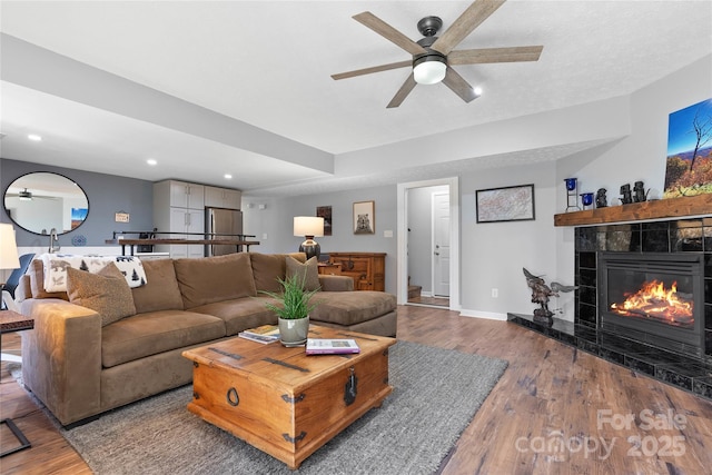 living area with a tile fireplace, recessed lighting, baseboards, and wood finished floors