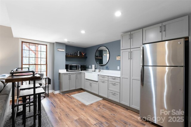 kitchen featuring gray cabinets, light countertops, light wood-style flooring, appliances with stainless steel finishes, and a sink