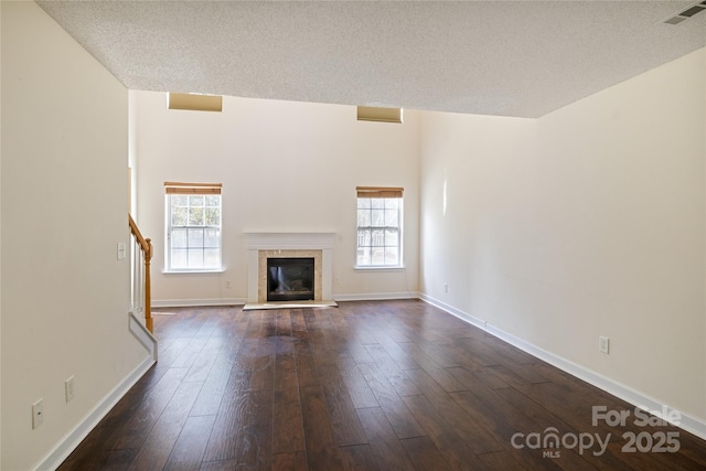 unfurnished living room featuring a healthy amount of sunlight, a textured ceiling, dark hardwood / wood-style floors, and a fireplace