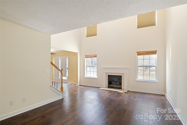 unfurnished living room with dark wood-type flooring, a textured ceiling, and a towering ceiling