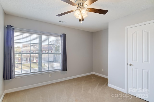 spare room featuring light carpet, ceiling fan, and a textured ceiling