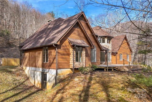 view of front of house featuring a shingled roof, a front yard, a wooden deck, and fence