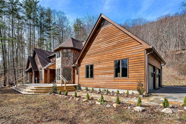 view of side of property featuring a porch, roof with shingles, driveway, and an attached garage