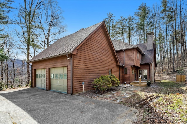 view of side of property featuring a shingled roof, a chimney, and a garage