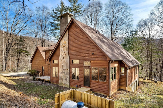 view of front facade with a shingled roof, a chimney, and a deck