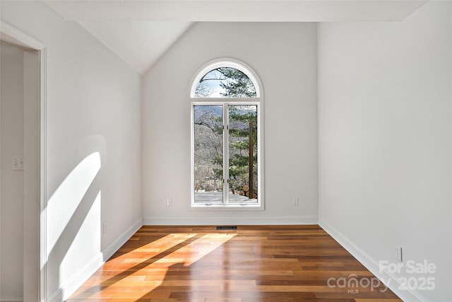 unfurnished room with lofted ceiling, visible vents, baseboards, and wood finished floors