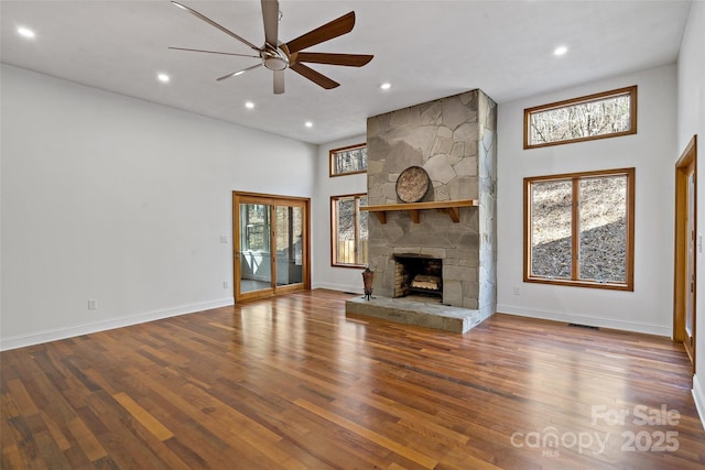 unfurnished living room with visible vents, a stone fireplace, baseboards, and wood finished floors