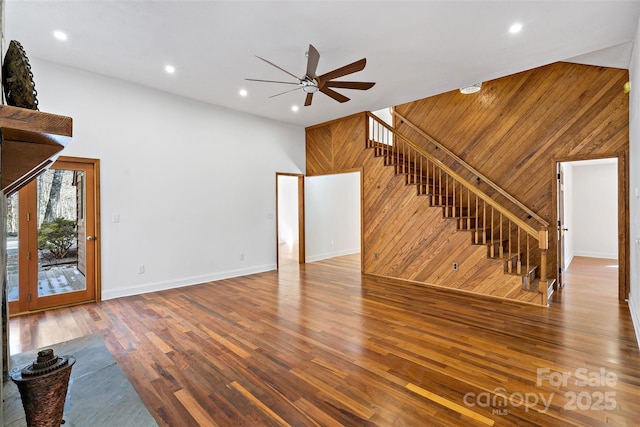 unfurnished living room with ceiling fan, wood finished floors, stairs, a high ceiling, and wood walls