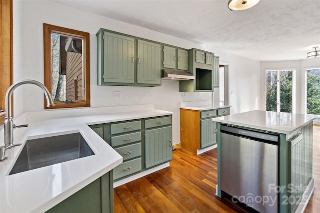 kitchen with under cabinet range hood, a sink, light countertops, stainless steel dishwasher, and green cabinetry