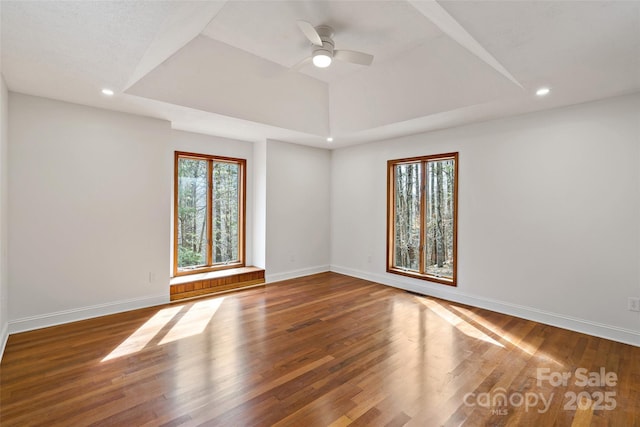 empty room featuring a tray ceiling, recessed lighting, baseboards, and wood finished floors