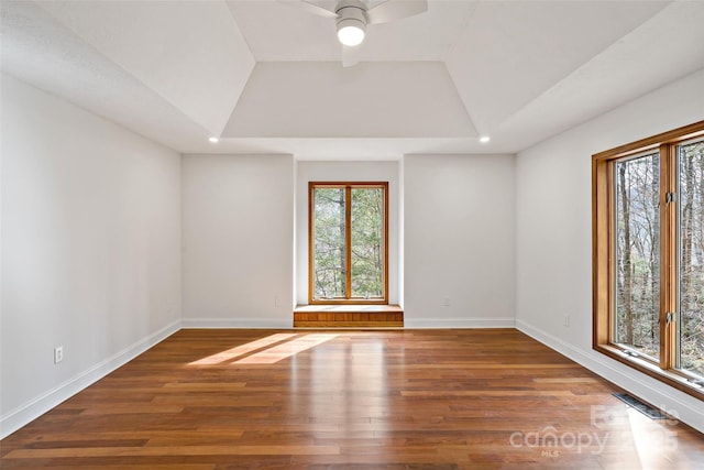 empty room featuring a tray ceiling, visible vents, plenty of natural light, and wood finished floors