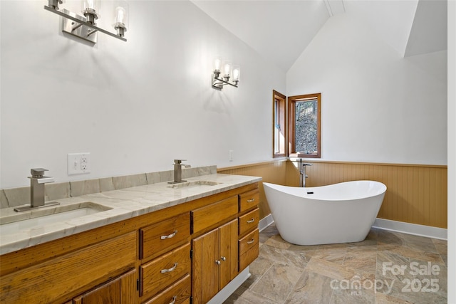 full bath with vaulted ceiling, a wainscoted wall, a sink, and a freestanding bath