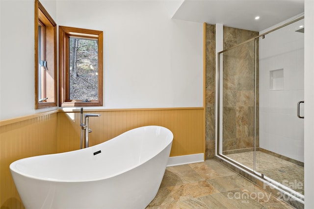 bathroom featuring a stall shower, wainscoting, a sink, wood walls, and a freestanding tub