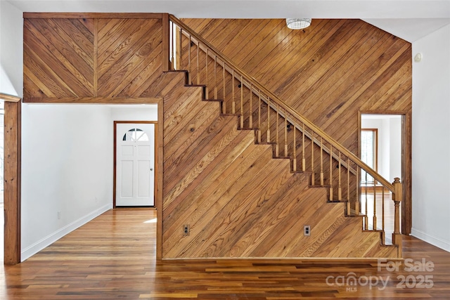 staircase featuring wood walls, wood finished floors, and baseboards