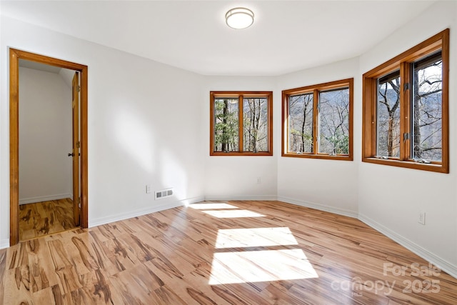 empty room with light wood-type flooring, visible vents, and baseboards