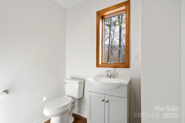 half bathroom featuring toilet, baseboards, and vanity