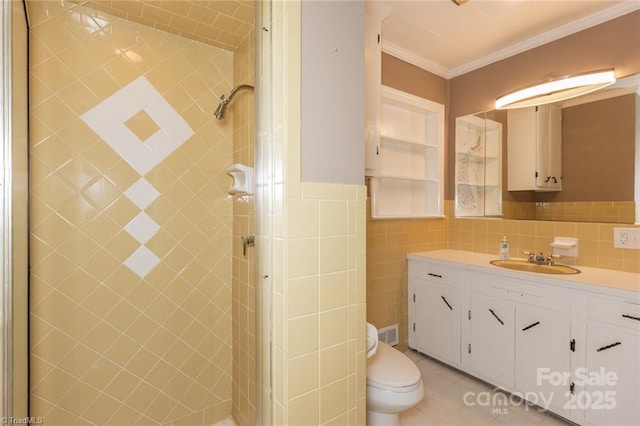 bathroom with tile walls, vanity, a tile shower, toilet, and ornamental molding