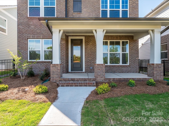 entrance to property featuring brick siding, a porch, and fence