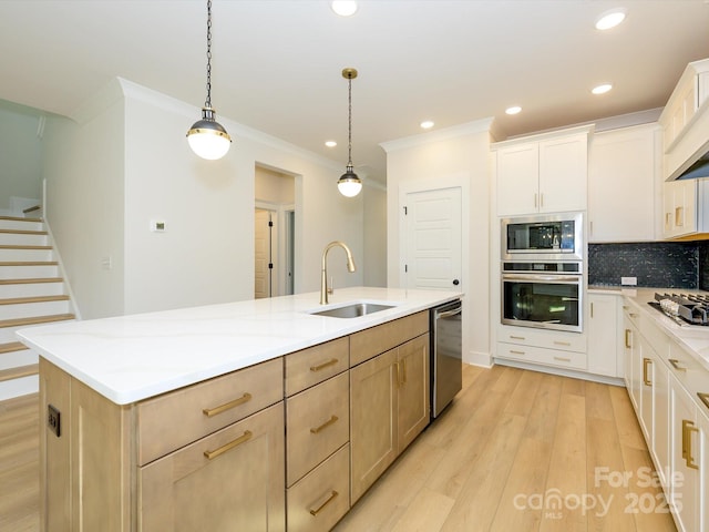 kitchen featuring light wood-style floors, a sink, stainless steel appliances, a center island with sink, and decorative backsplash