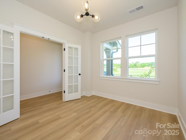 spare room featuring baseboards, light wood-type flooring, a chandelier, french doors, and visible vents