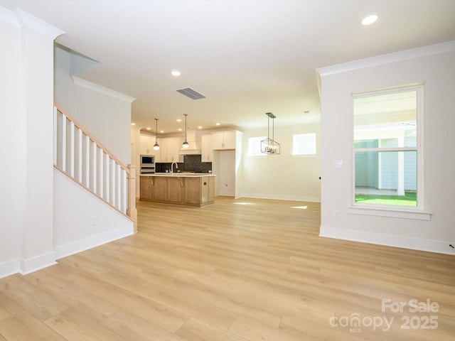 unfurnished living room featuring crown molding, visible vents, stairway, a sink, and baseboards