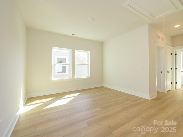 spare room with attic access, visible vents, light wood-type flooring, and baseboards