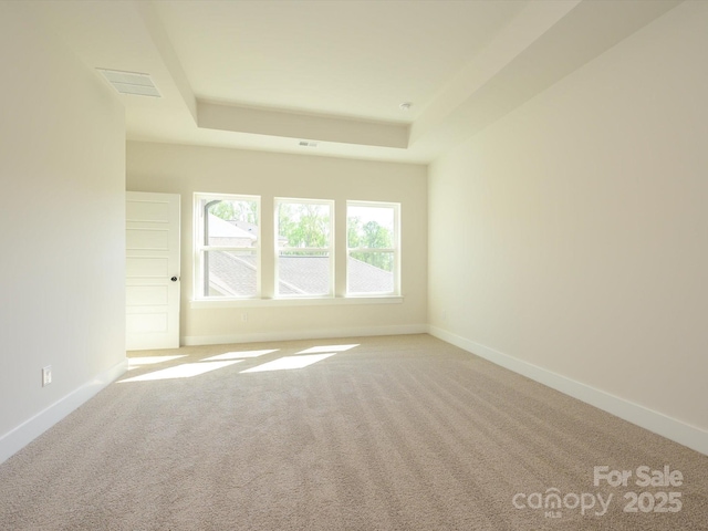 spare room featuring a tray ceiling, light colored carpet, and baseboards