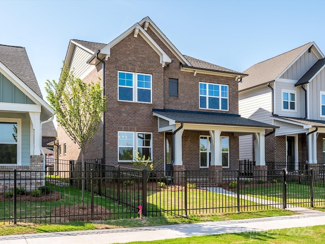 craftsman-style home featuring roof with shingles, a fenced front yard, a front lawn, and brick siding