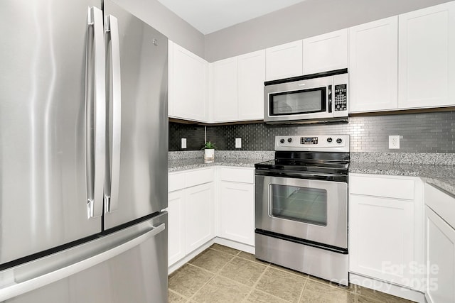 kitchen featuring stainless steel appliances, white cabinets, light stone counters, and tasteful backsplash