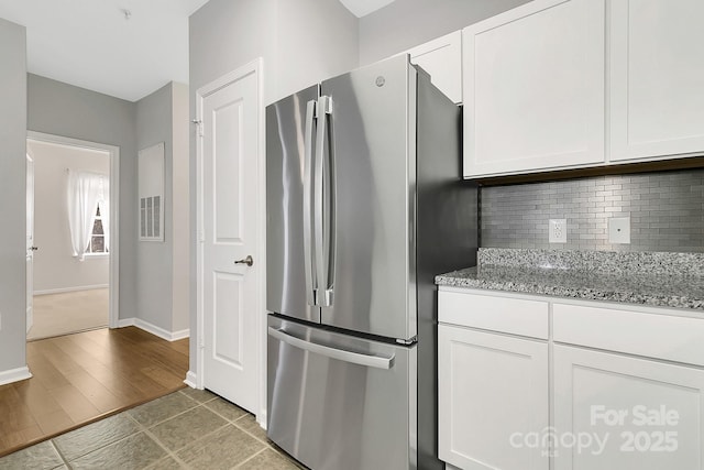 kitchen with baseboards, white cabinets, backsplash, freestanding refrigerator, and light stone countertops