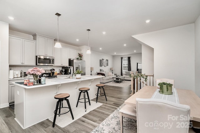 kitchen featuring pendant lighting, light countertops, appliances with stainless steel finishes, an island with sink, and a kitchen breakfast bar