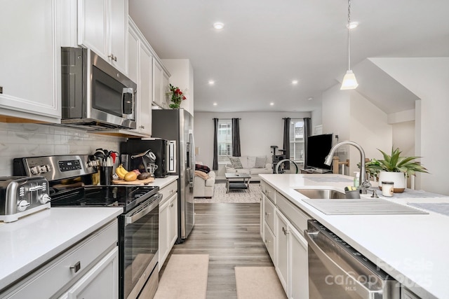 kitchen featuring stainless steel appliances, white cabinetry, open floor plan, light countertops, and pendant lighting