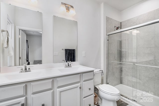 full bath featuring double vanity, a stall shower, a sink, and toilet