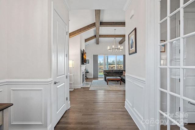 entrance foyer featuring dark wood-style flooring, a wainscoted wall, a notable chandelier, a decorative wall, and lofted ceiling with beams