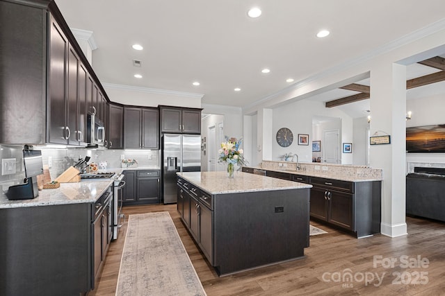 kitchen with light stone counters, a center island, decorative backsplash, appliances with stainless steel finishes, and a peninsula