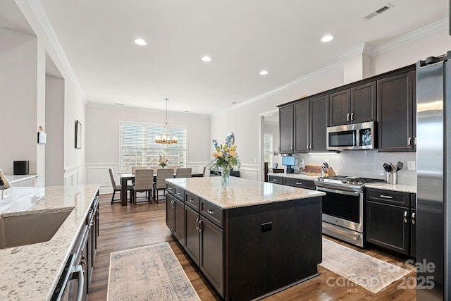 kitchen featuring light stone counters, stainless steel appliances, a kitchen island, visible vents, and decorative light fixtures