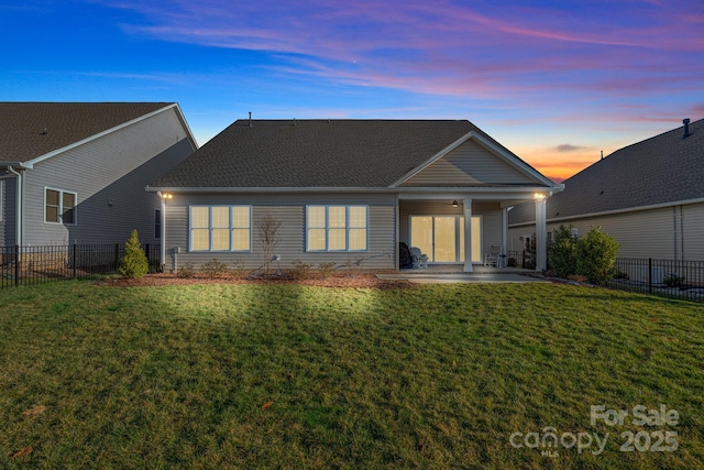 back of property at dusk with a patio area, a lawn, and fence