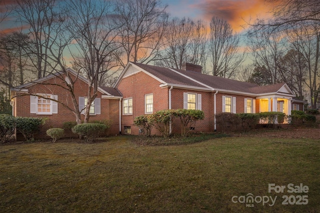 view of front facade with a chimney, a lawn, brick siding, and crawl space