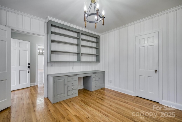 unfurnished office with an inviting chandelier, crown molding, light wood-style floors, built in shelves, and built in desk