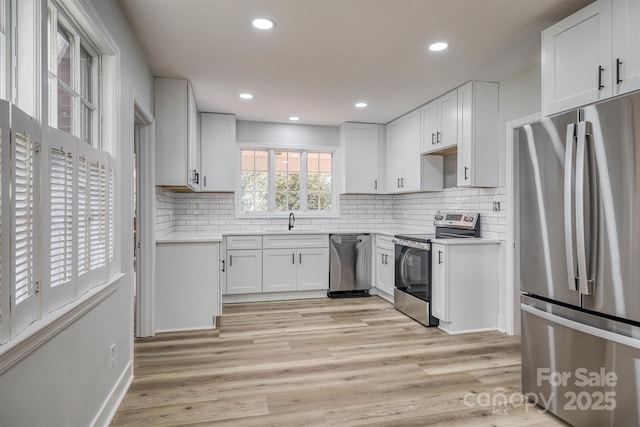 kitchen featuring stainless steel appliances, light wood-type flooring, a sink, and backsplash