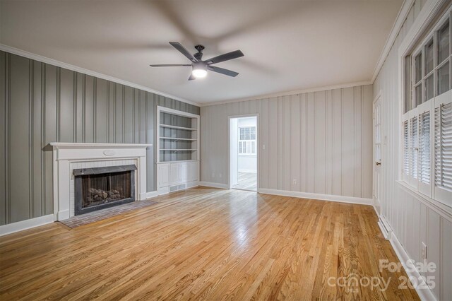 unfurnished living room featuring baseboards, built in features, ornamental molding, wood finished floors, and a fireplace