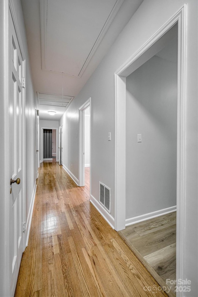 hallway with light wood-style floors, attic access, visible vents, and baseboards