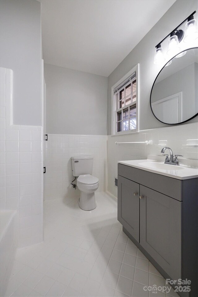 full bath featuring wainscoting, toilet, tile patterned floors, vanity, and tile walls