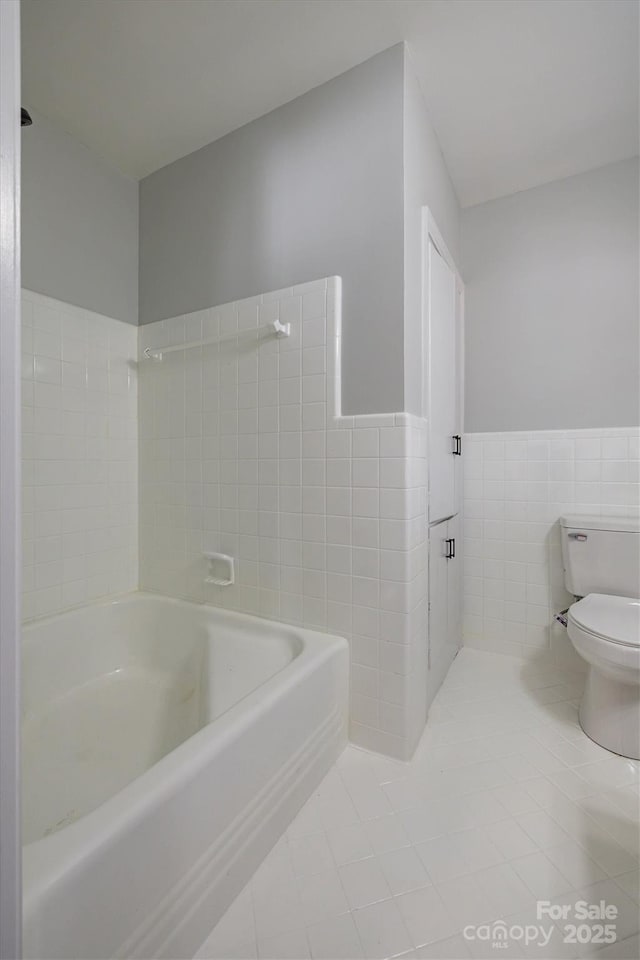 bathroom with toilet, a wainscoted wall, tile patterned flooring, and tile walls