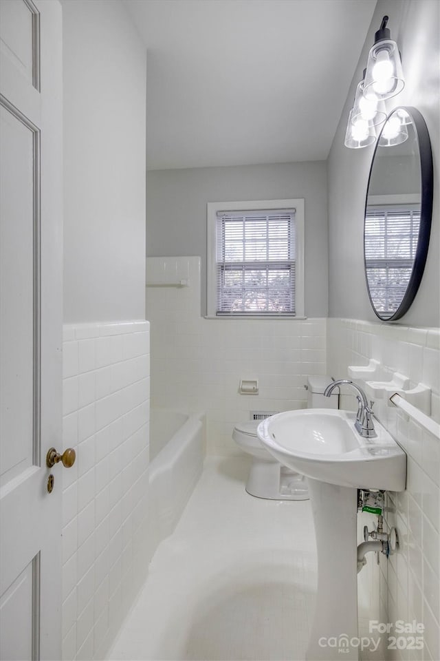 bathroom featuring a washtub, wainscoting, toilet, and tile walls