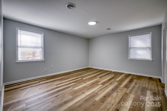 unfurnished room featuring wood finished floors, visible vents, and baseboards